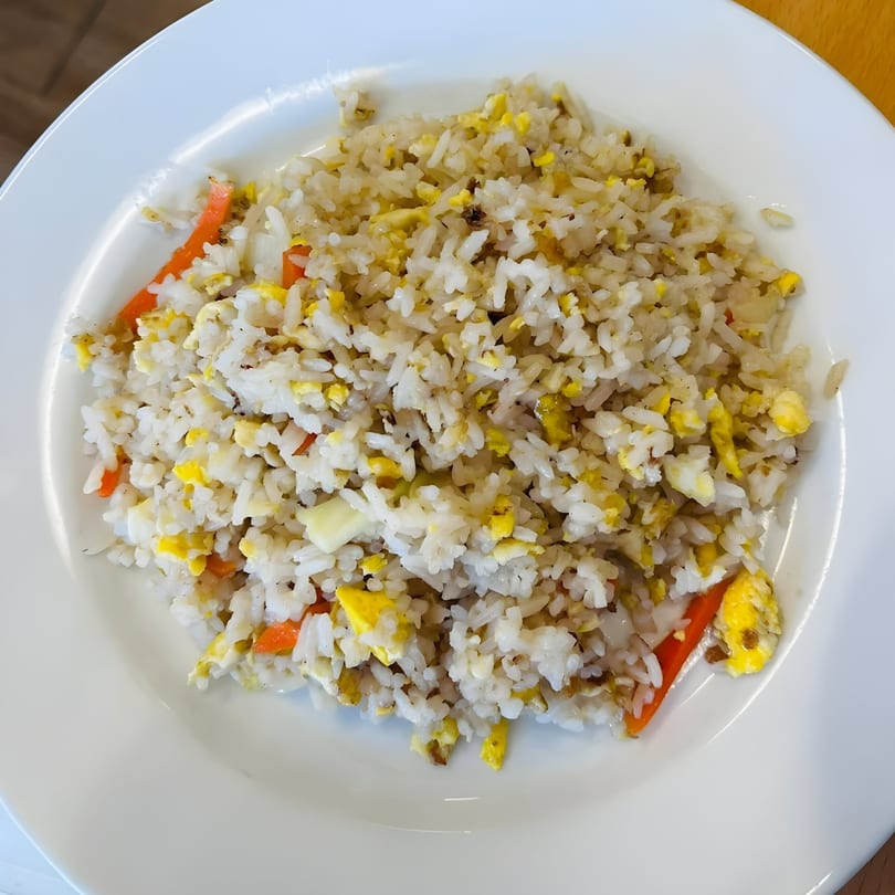 A white plate filled with Thai fried rice, featuring white rice, scrambled egg, and carrots.